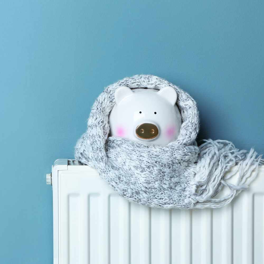 Piggy bank with warm scarf on heating radiator near color wall